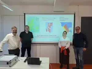 Asger Brandt, Jesper Buchhold Gjørup, Eva-Maria Euchner und Christoph Hohage stehen vor einer Präsentation auf der die Kooperation zwischen der Fliedner Fachhochschule und der Via University College - Campus Holstebro verdeutlicht wird