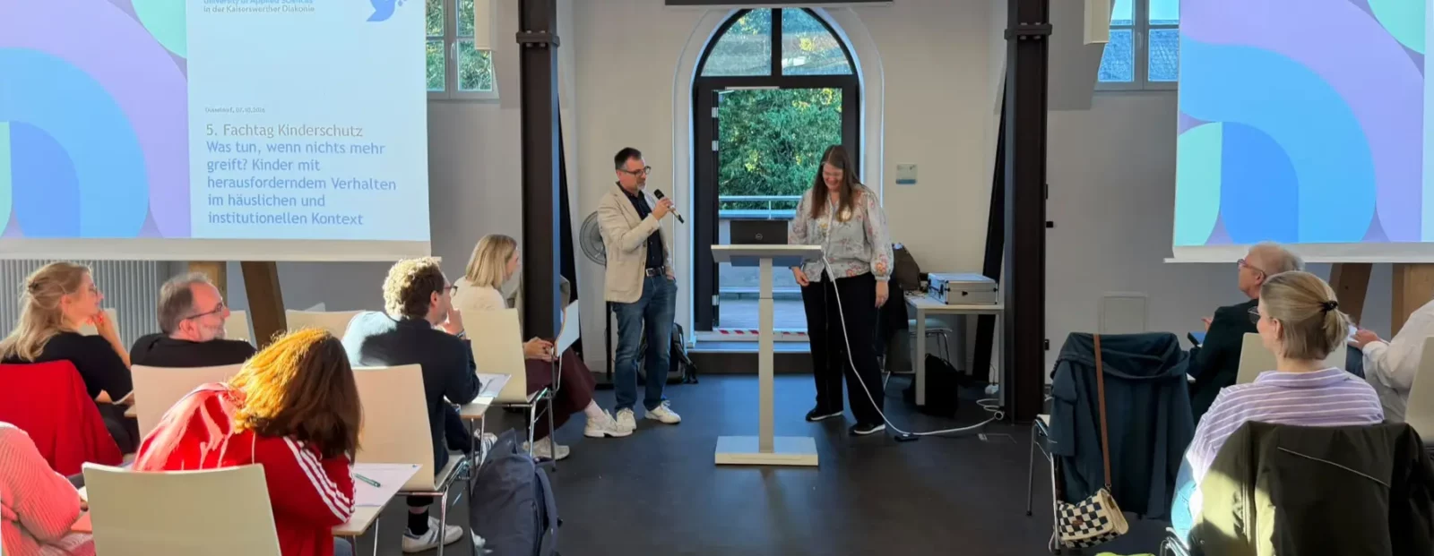 Plenum vom 5. Fachtag Kinderschutz im Luise-Fliedner-Saal der Fliedner Fachhochschule. Prof. Dr. Bernd Hemming und Prof. Dr. Sonja Damen sprechen mit den Teilnehmenden.