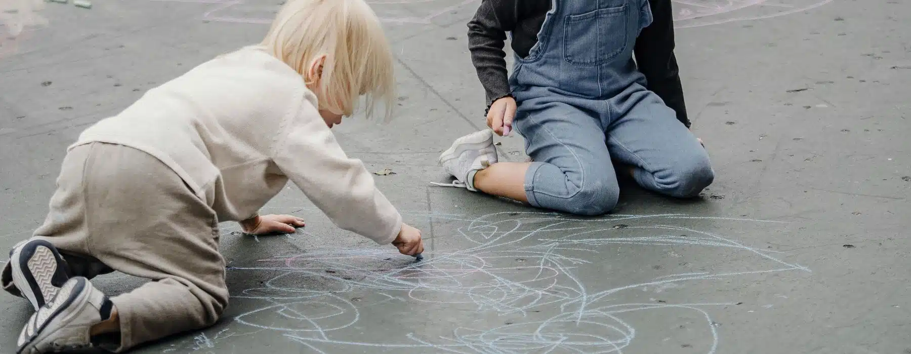 Zwei Kinder malen mit bunter Kreide auf dem Asphalt