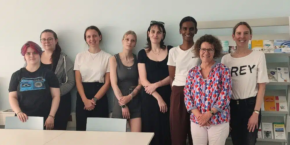 Acht Personen, darunter Studierende, stehen in einem Raum mit Regalen voller medizinischer Produkte.